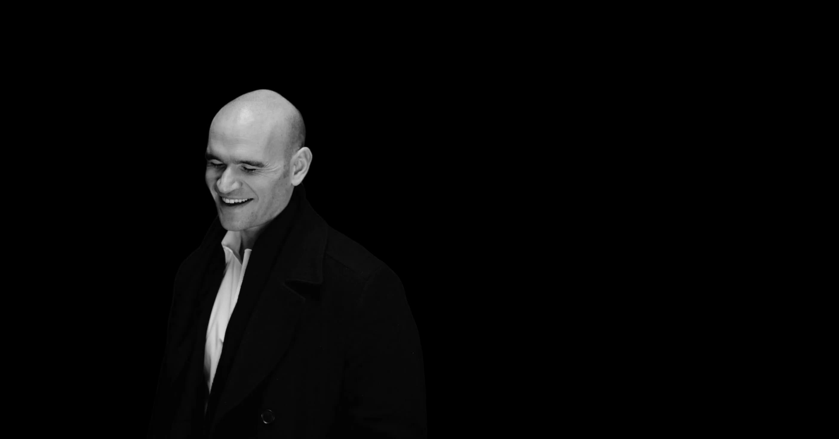 Michael Fabiano in an overcoat, smiling, photographed in black and white