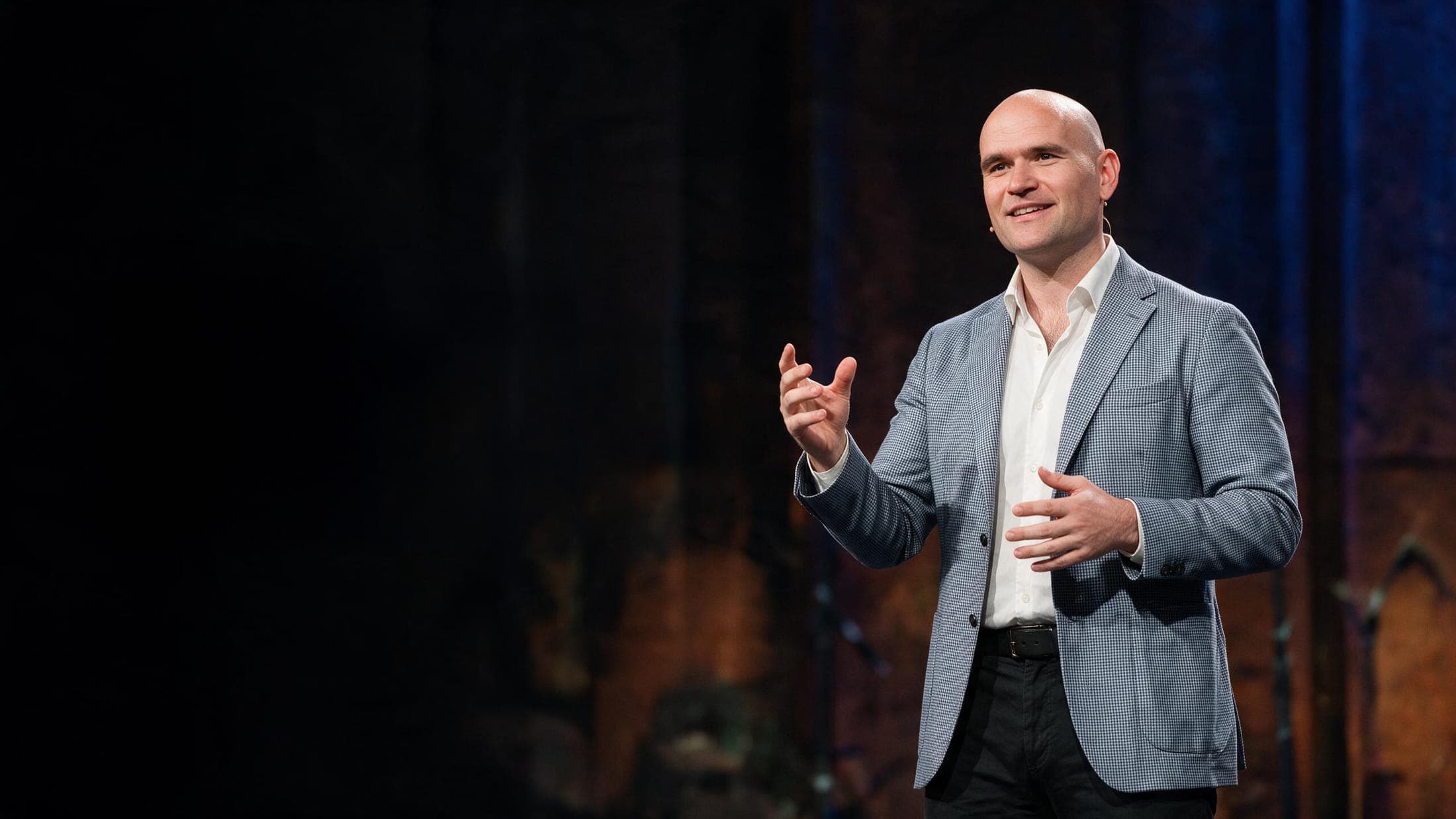 Michael Fabiano speaking on a darkened stage, mid-gesture under a spotlight
